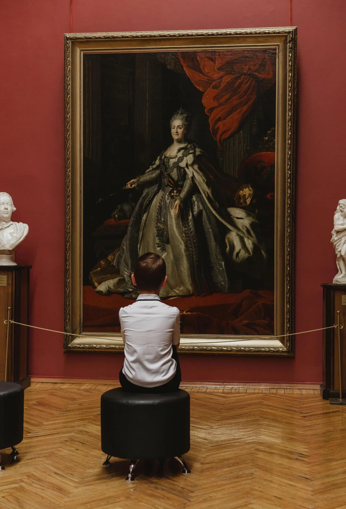 A young student sits and studies a classical oil portrait in a museum gallery